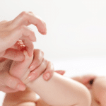 Femme en train de pratiquer un modelage bébé sur les pieds de celui-ci.